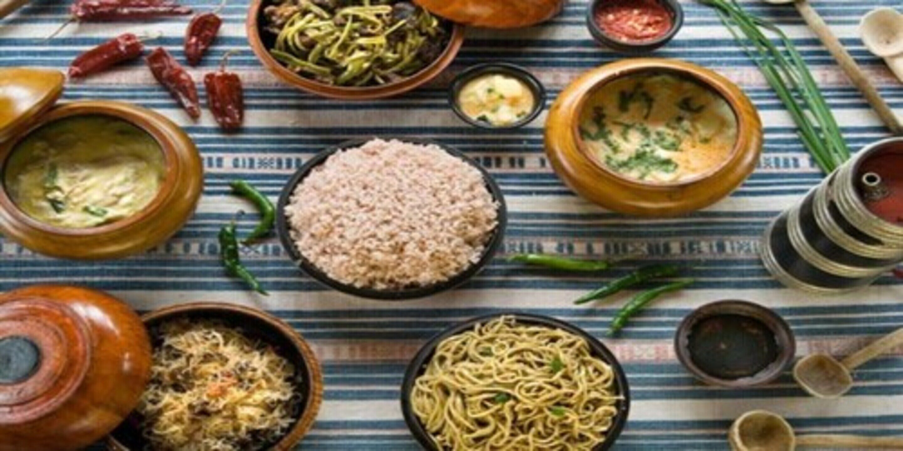 A variety of dishes including rice, noodles, and a bowl of soup, arranged on a striped tablecloth.
