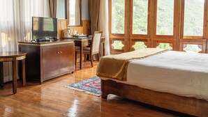 A wooden room with a bed, a desk with a television, and large windows. - Tiger Nest Resort (Paro)