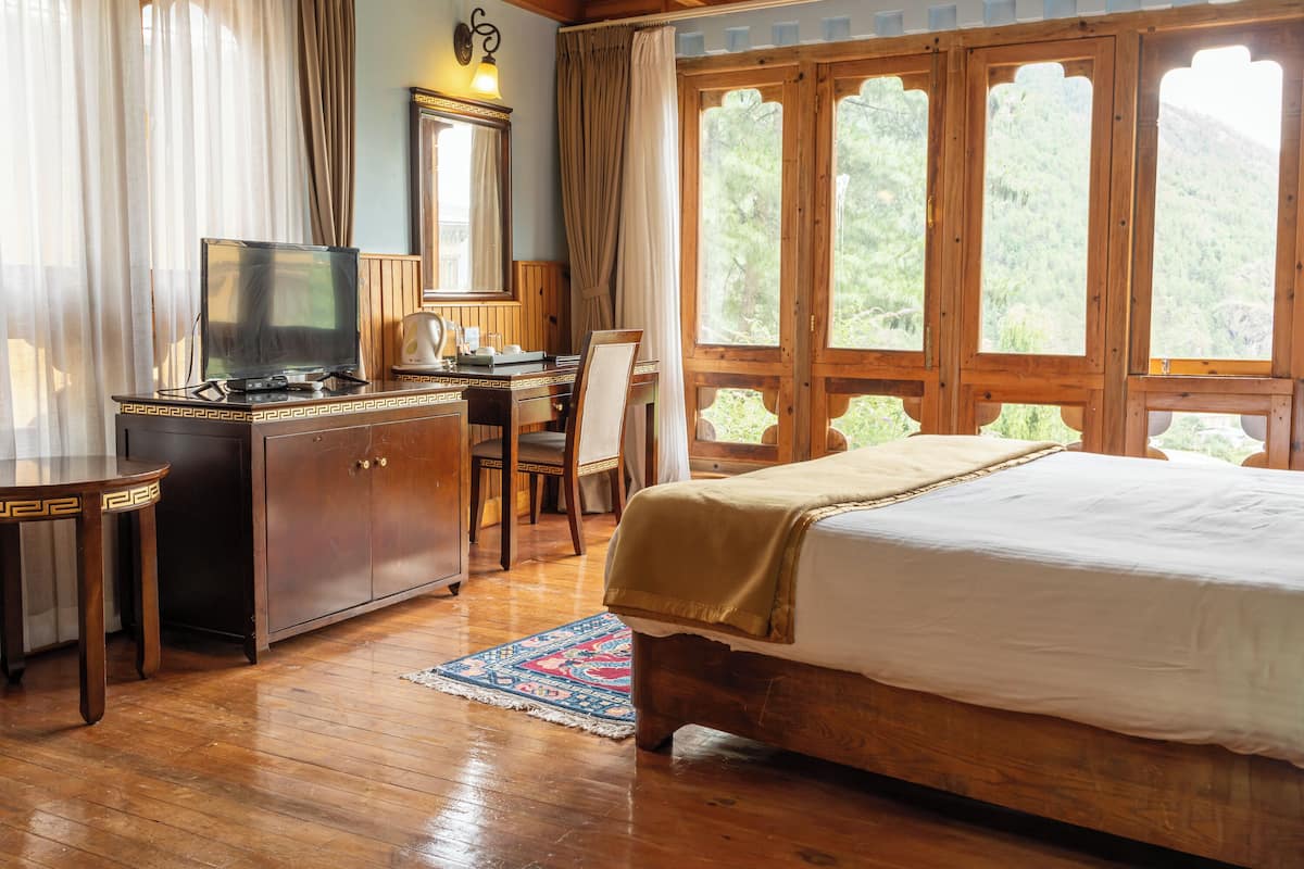 A wooden room with a bed, a desk with a television, and large windows.