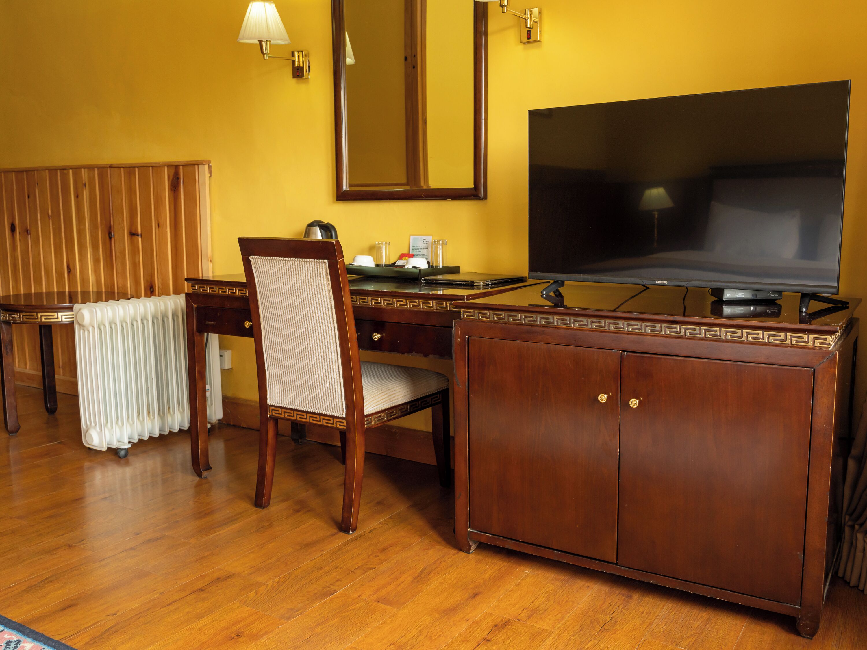 A hotel room with a wooden desk, a chair, a television, and a mirror.