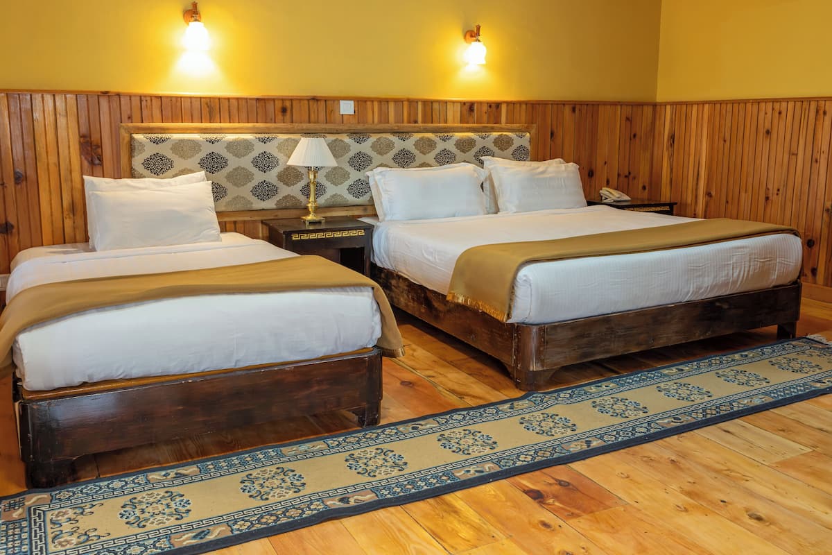 A room with two wooden beds, a patterned rug, and two wall-mounted lamps.