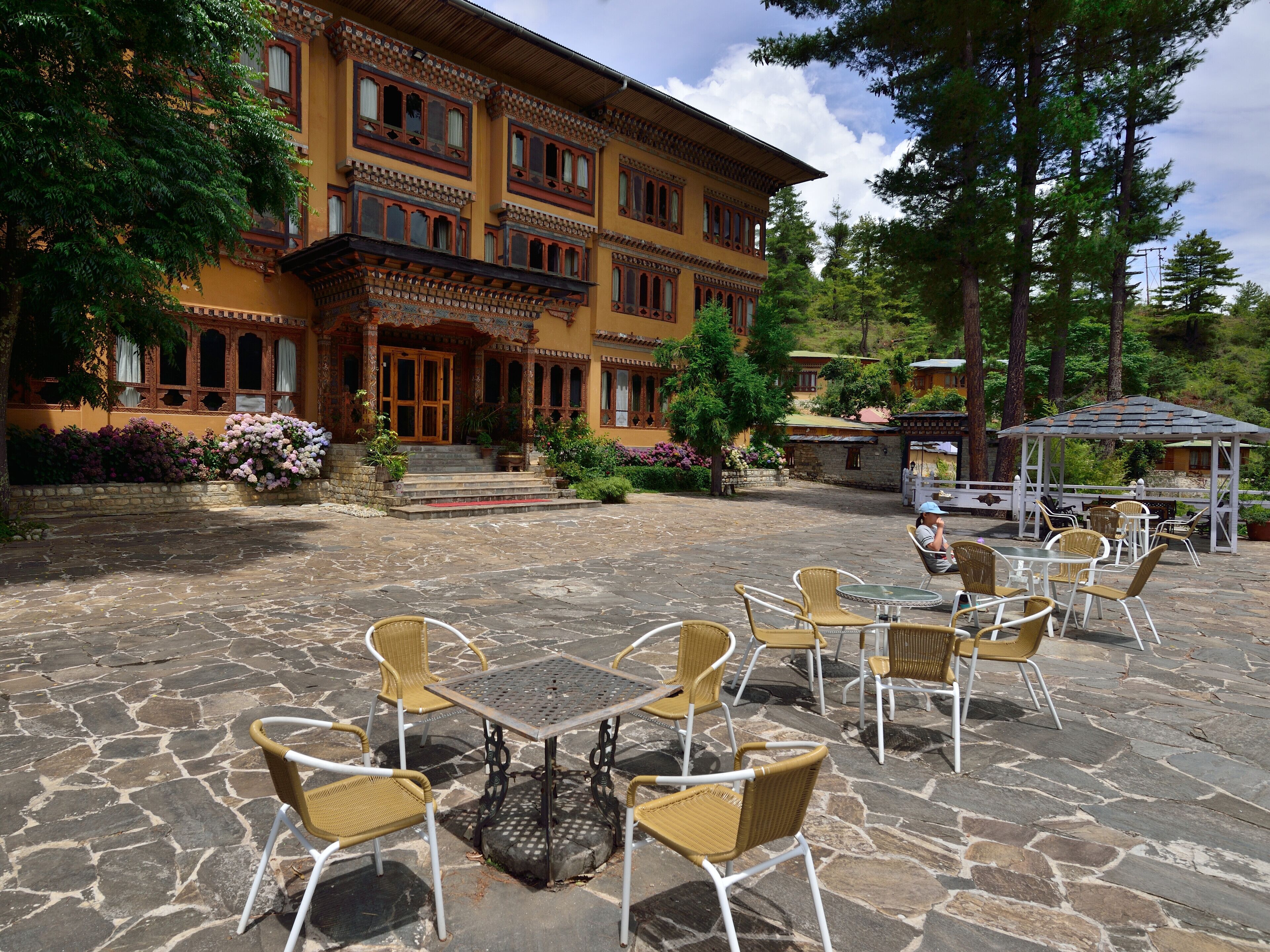 A courtyard with stone flooring and wicker chairs, a building with ornate architecture, and a gazebo.