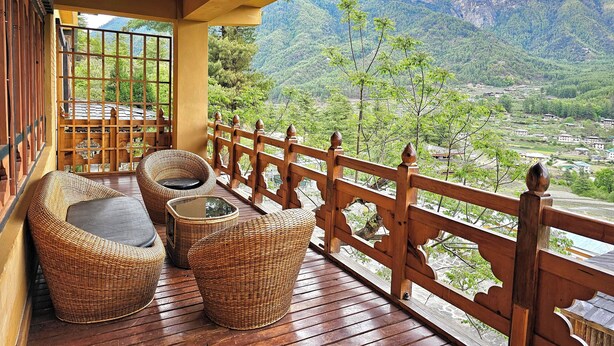 A wooden deck with wicker furniture and a view of a mountainous landscape. - Tiger Nest Resort (Paro)