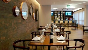 A restaurant with brick walls, clocks, and a bar area in the background. - Gran Executive Hotel (Uberlandia)