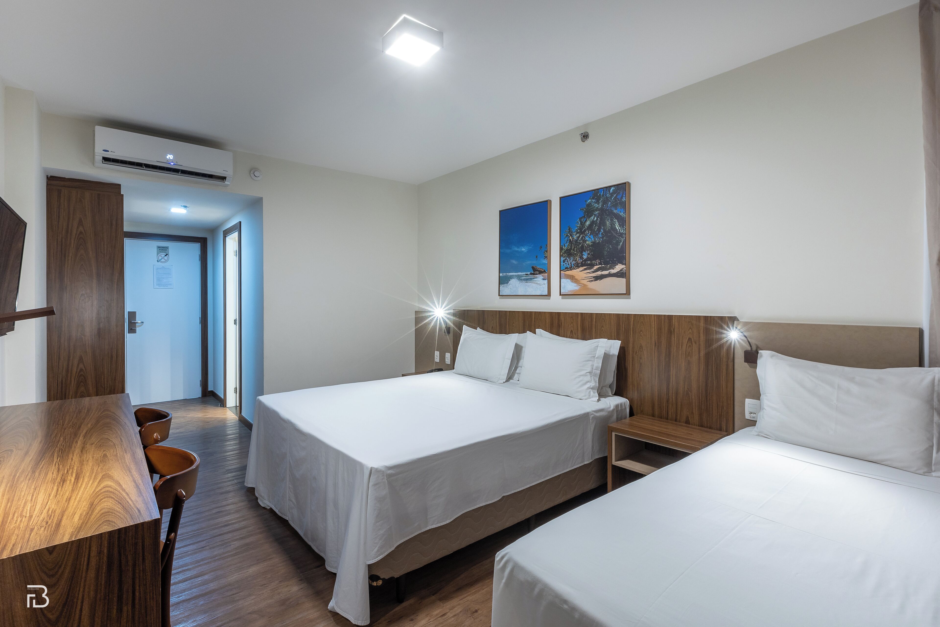 A hotel room with two beds, a wooden desk, and a view of the beach.
