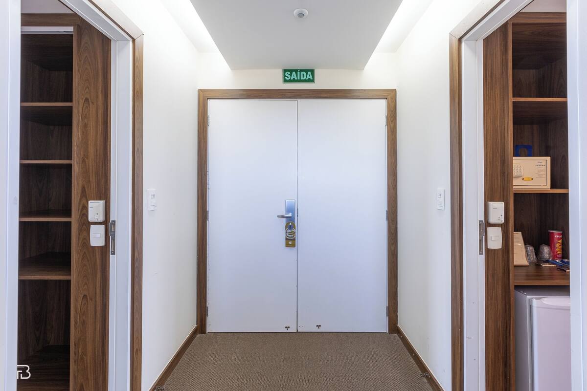 A hallway with a double door, a sign above the door, and a small shelf with items on the right.