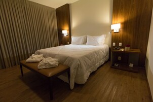 Una habitación de hotel con una cama grande, mesitas de noche, un banco y suelo de madera.