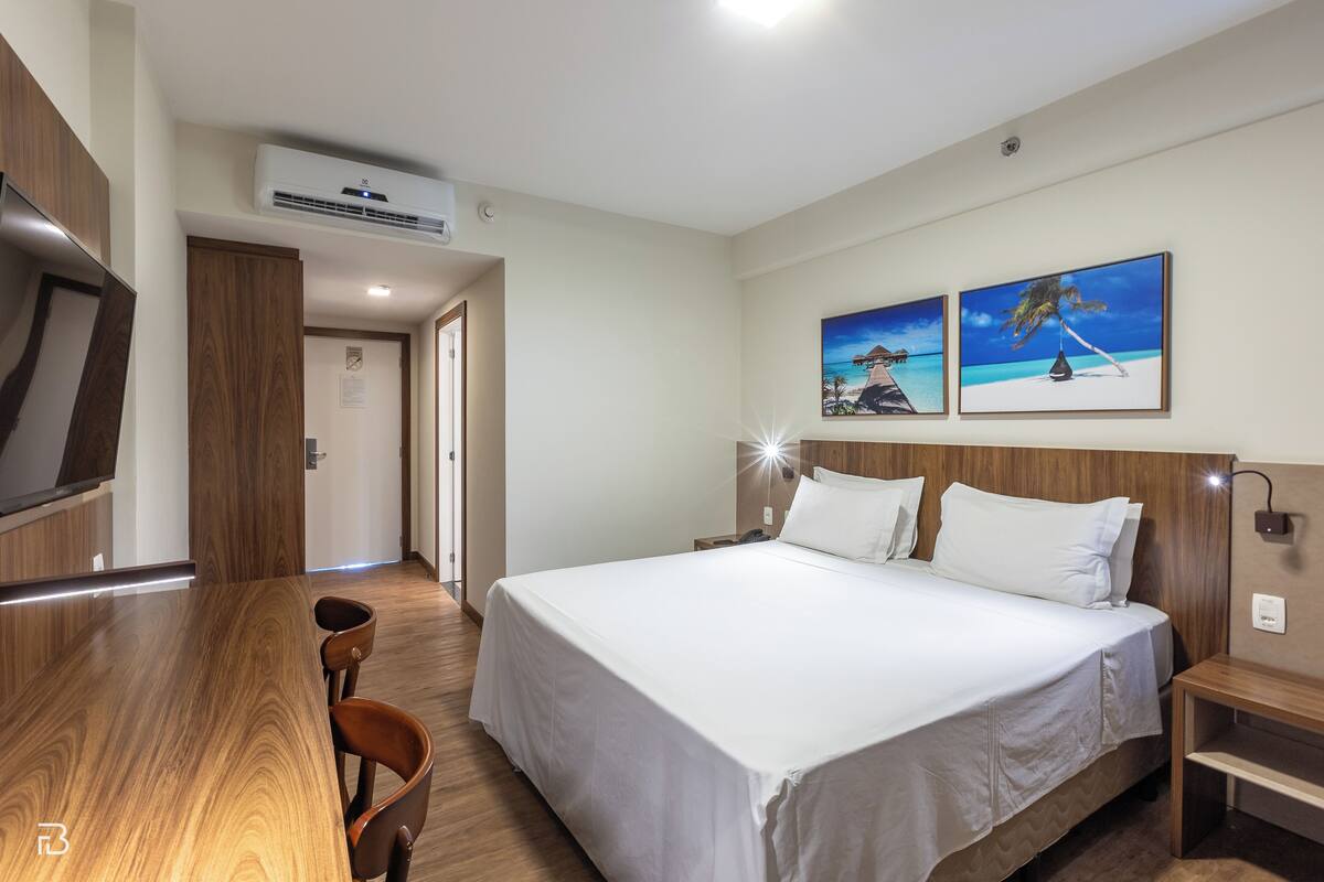 A hotel room with a large bed, a wooden desk, and two paintings on the wall.