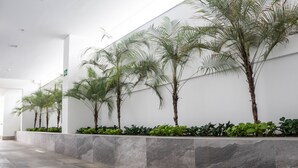 A modern interior with a long hallway lined with palm trees and low green plants. - Gran Executive Hotel (Uberlandia)