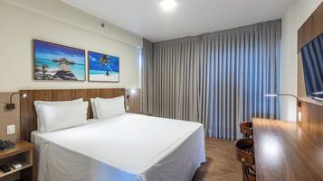 A hotel room with a large bed, a desk with a chair, a telephone, and two paintings on the wall.
