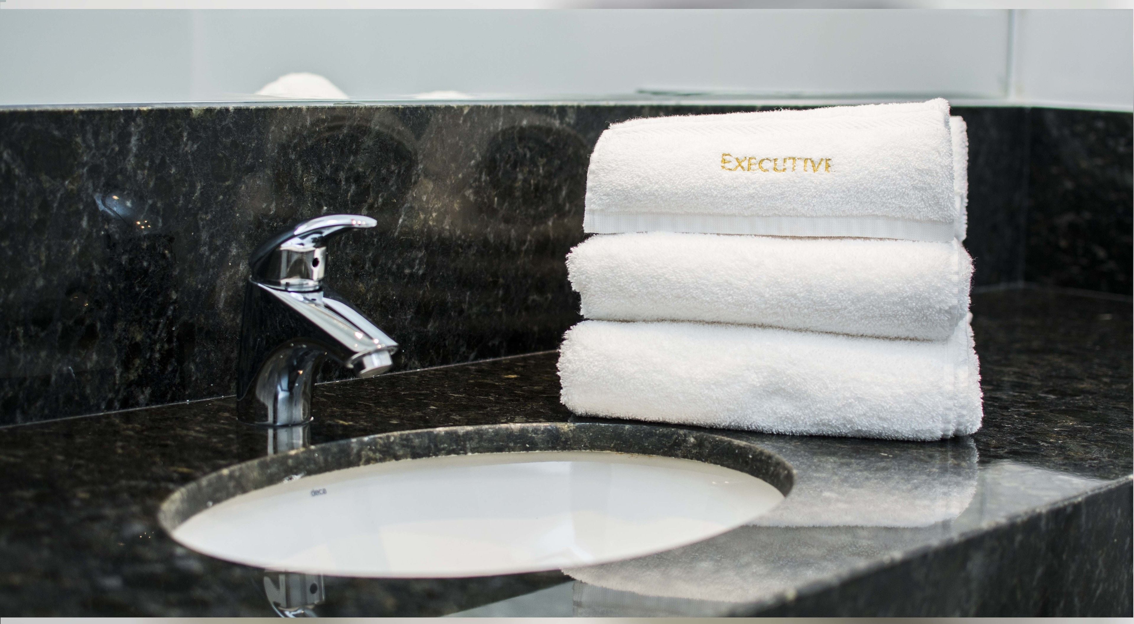 A bathroom with a black marble countertop, a chrome faucet, and a stack of white towels with "EXECUTIVE" embroidered on them.