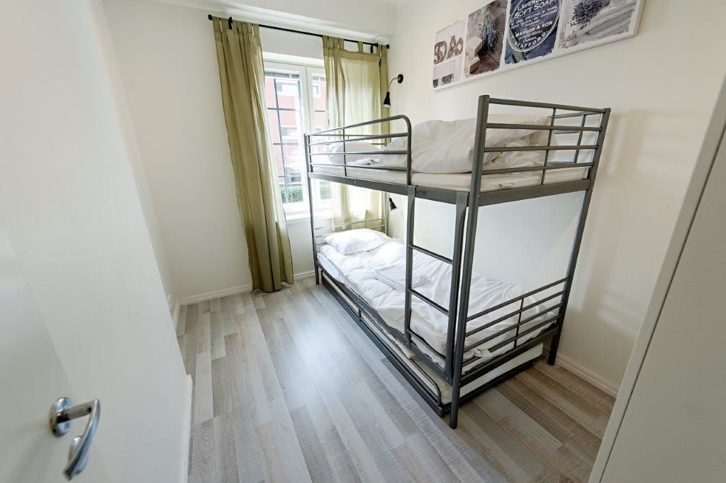 A bunk bed room with a window, curtains, and a door.