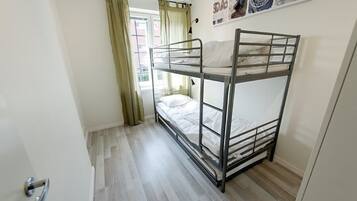 A bunk bed room with a window, curtains, and a door.