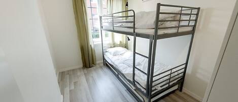 A bunk bed room with a window, curtains, and a door.