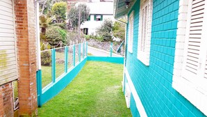 Un espace extérieur étroit et clos, avec une pelouse verdoyante, un mur de briques et une clôture bleue.