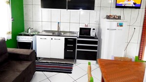 Une cuisine compacte équipée d’une cuisinière à gaz, d’un four à micro-ondes et d’un petit réfrigérateur. Un téléviseur est fixé au mur, et un canapé et une table à manger se trouvent dans le salon adjacent.