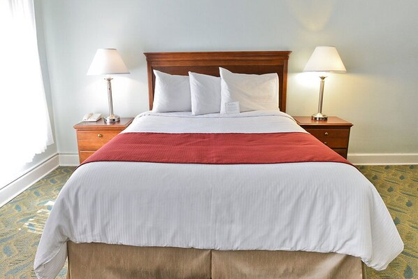 A neatly made bed with a wooden headboard, two bedside tables with lamps, and a patterned carpet. - Penn Wells Historic Hotel (Wellsboro)