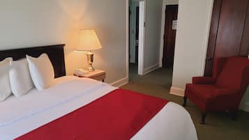 Habitación de hotel con una cama bien hecha, una lámpara, una silla y una puerta que da a otra habitación.