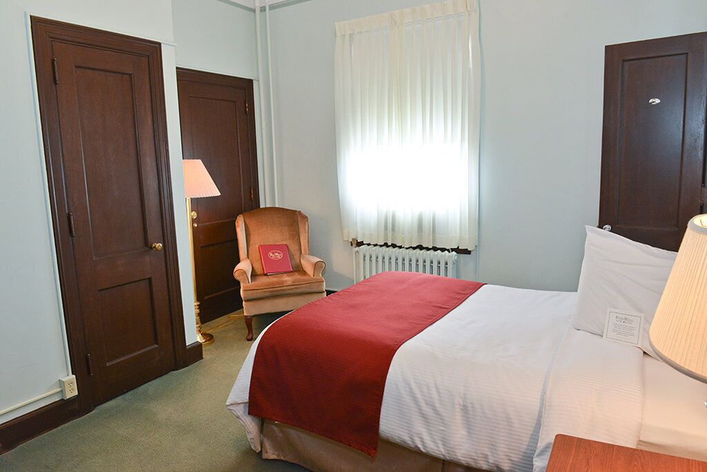A hotel room with a bed, a chair, a window with curtains, and a radiator.