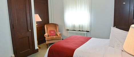 A hotel room with a bed, a chair, a window with curtains, and a radiator.