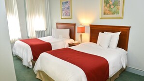 Een hotelkamer met twee bedden, elk met een rood-witte dekbedovertrek, een houten hoofdbord, een bedlampje en een ingelijste foto aan de muur.
