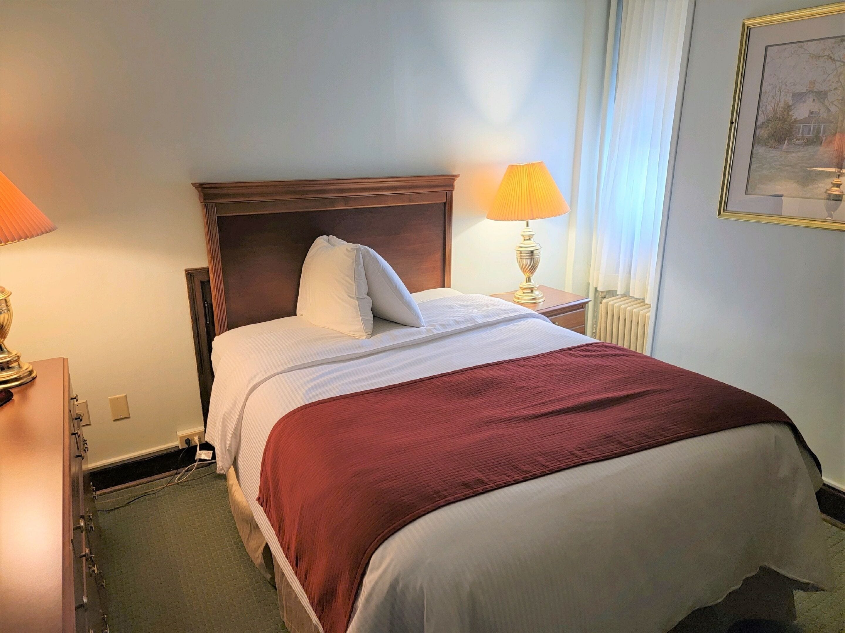 Una cama bien hecha con cabecera de madera, una manta roja y una lámpara de noche.