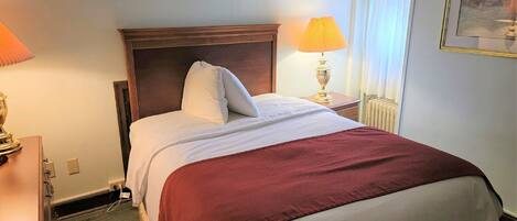 Una cama bien hecha con cabecera de madera, una manta roja y una lámpara de noche.