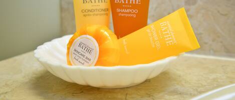 A white ceramic dish containing three toiletries: a yellow conditioner, an orange shampoo, and a white shower gel.