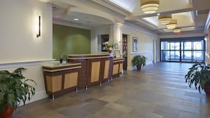 Een ruime lobby met een receptiebalie, grote ramen en een hoge plafond met hangende verlichting.