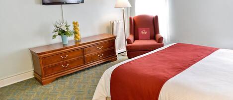 Une chambre d’hôtel avec un lit, une commode en bois, un fauteuil rouge, une télévision et une lampe.