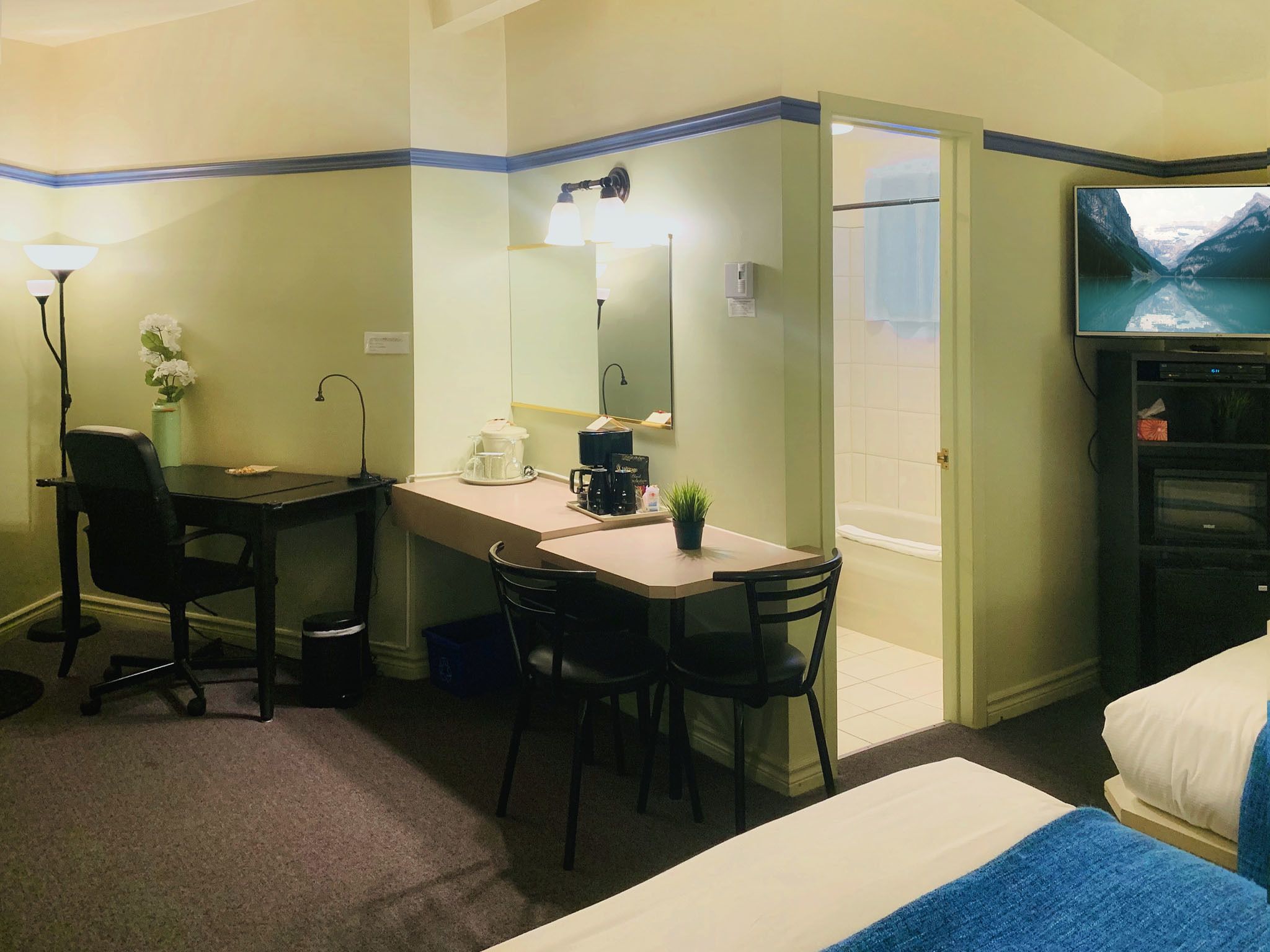 Habitación de hotel con escritorio, dos sillas, una cama, televisión y baño con bañera.