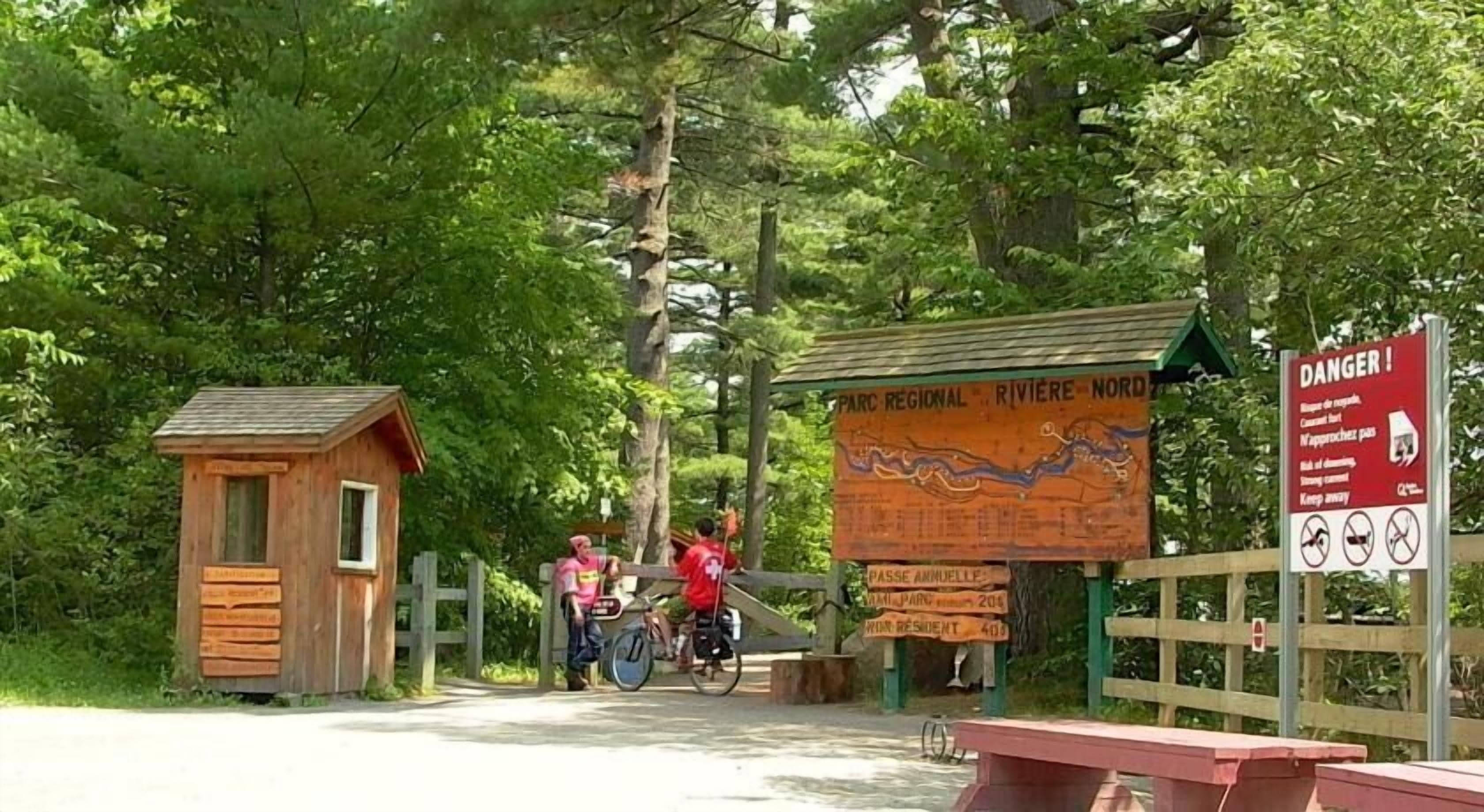 Una cabaña de madera, un letrero de madera con un mapa, y un letrero de 'Peligro' con prohibiciones.