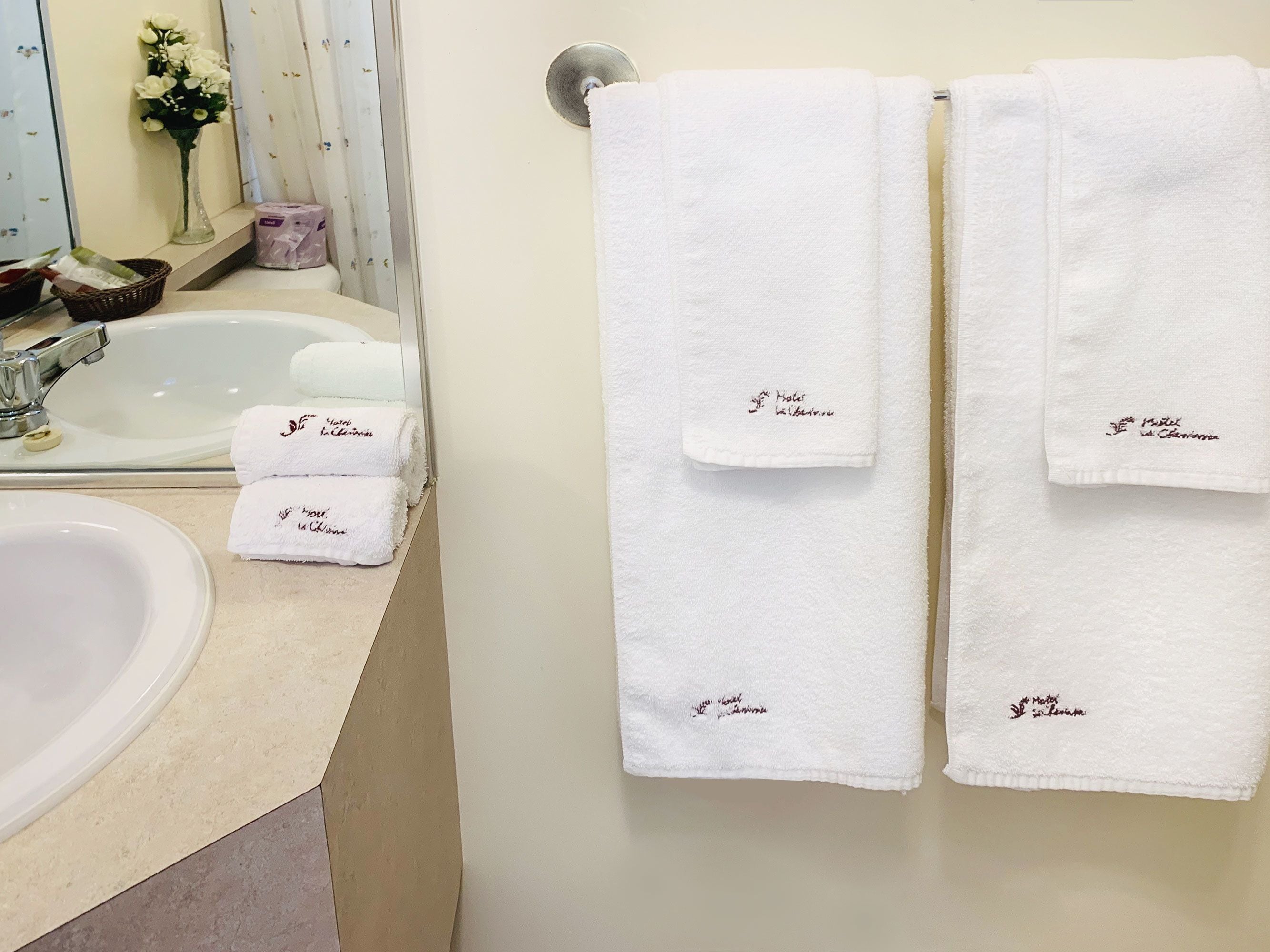 Une salle de bain avec un lavabo, deux serviettes suspendues à un porte-serviettes et un vase de fleurs posé sur le comptoir.