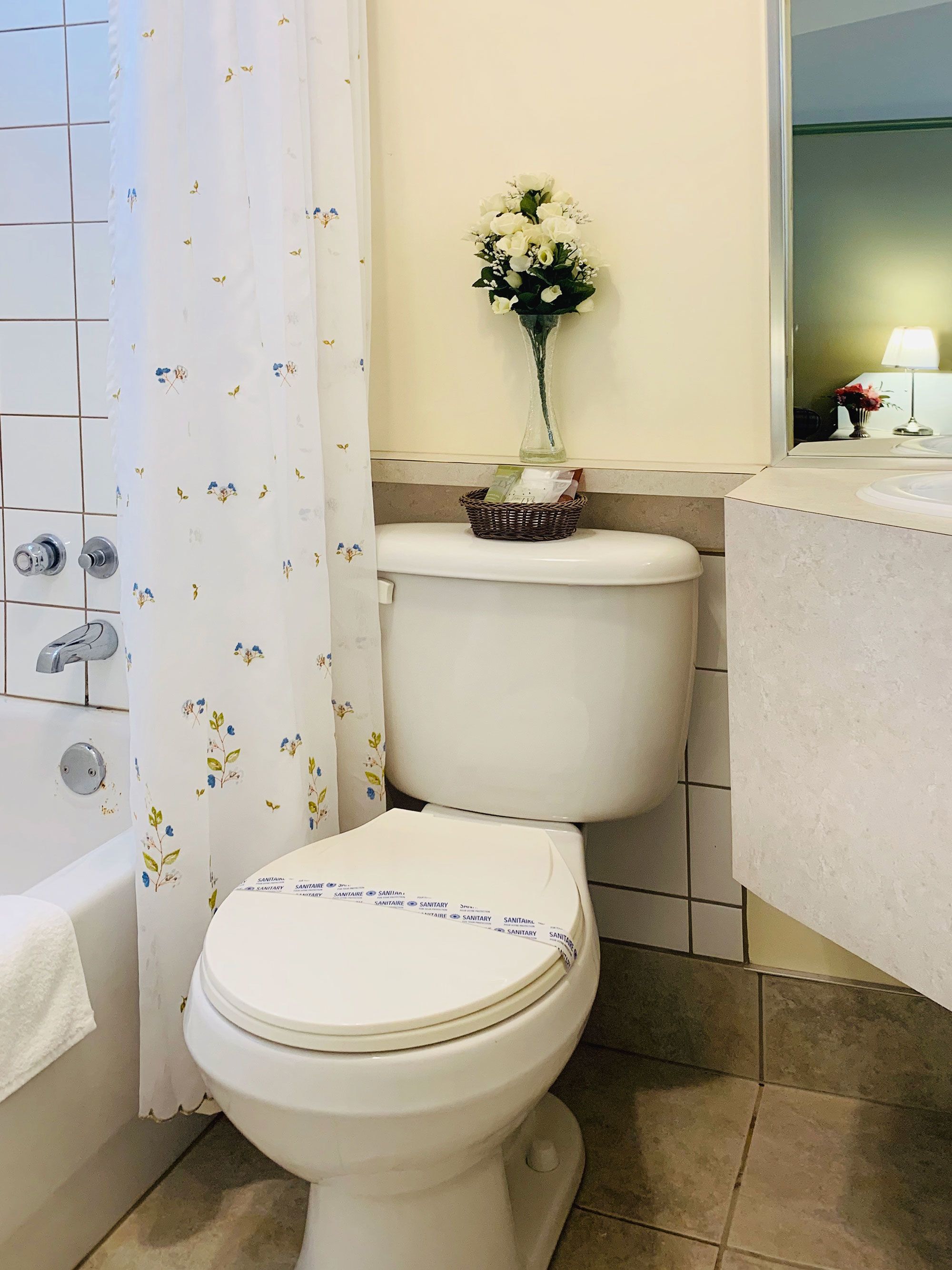 A bathroom with a toilet, a shower curtain, a vase with flowers, and a sink.