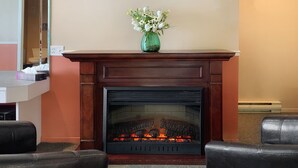 Una chimenea encendida, dos sillones de cuero, un florero con flores y un espejo en la pared.