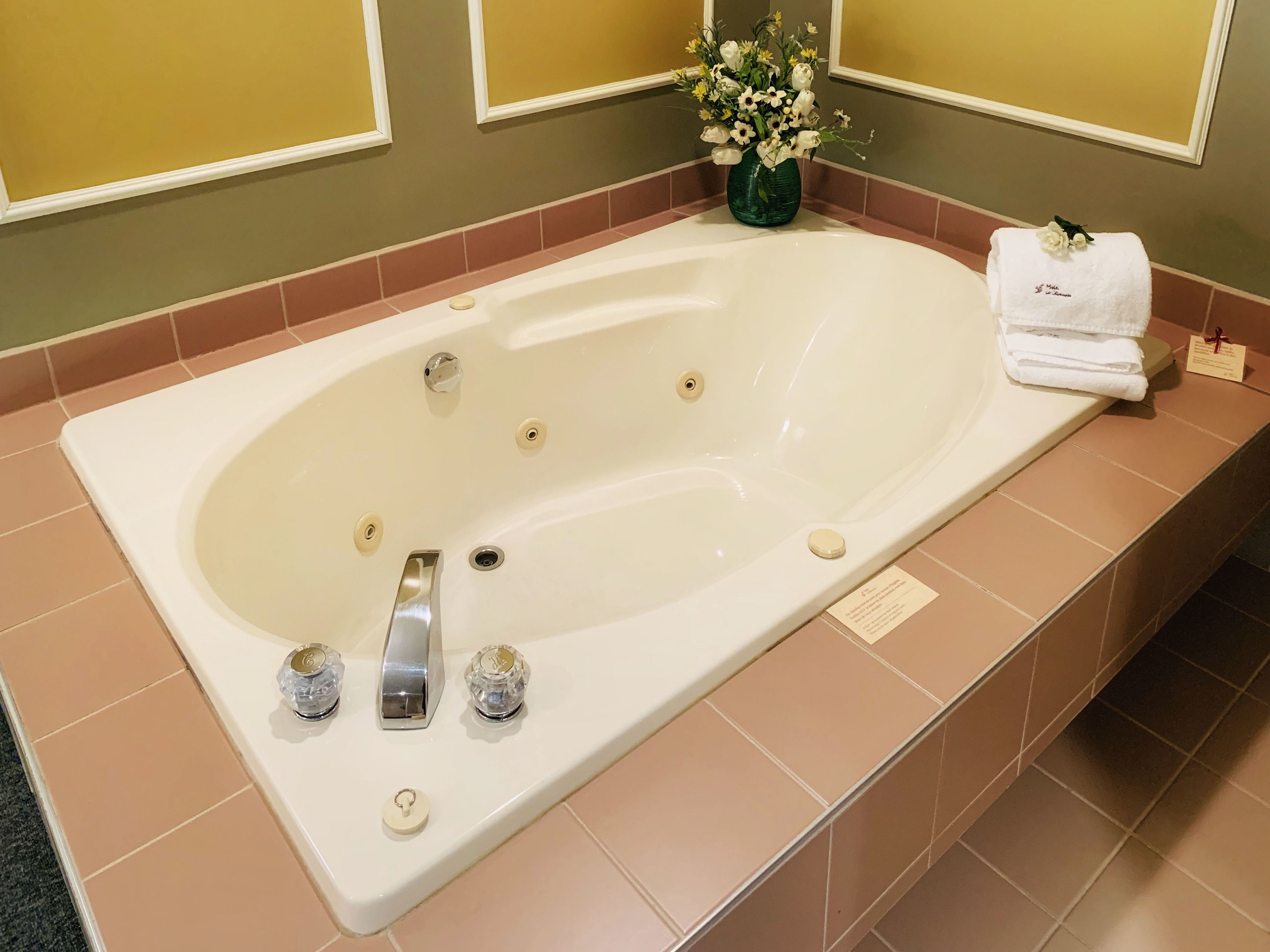 A large bathtub with multiple faucets, a flower vase, and a towel on the side.