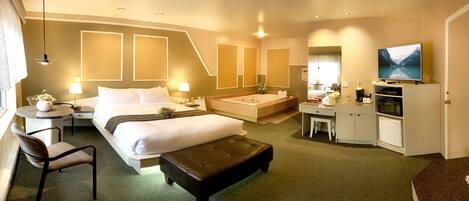A hotel room with a bed, a desk, a chair, a small table, a sofa, a TV, a bathroom with a bathtub, and a mirror.