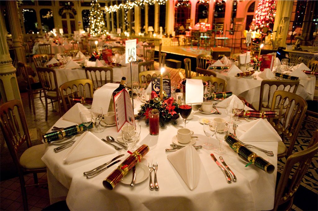 A formal dining room with round tables set for a meal, each with a menu stand, glasses, and cutlery.