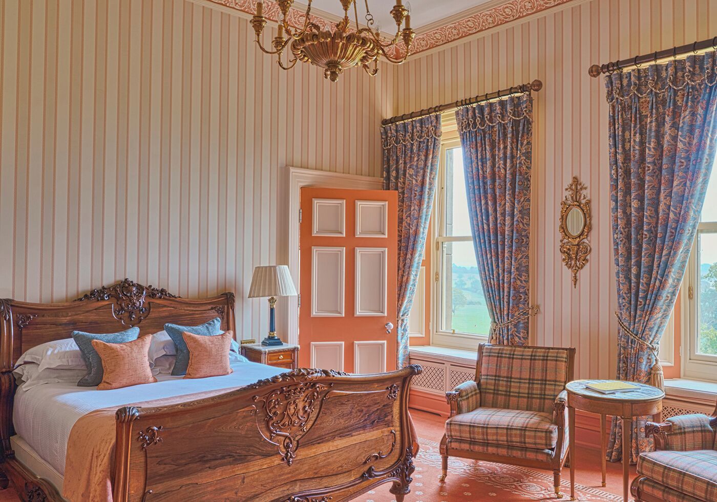 A spacious bedroom with a large bed, a chair, a small table, and a window with curtains.