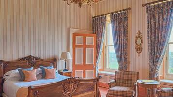 A spacious bedroom with a large bed, a chair, a small table, and a window with curtains.