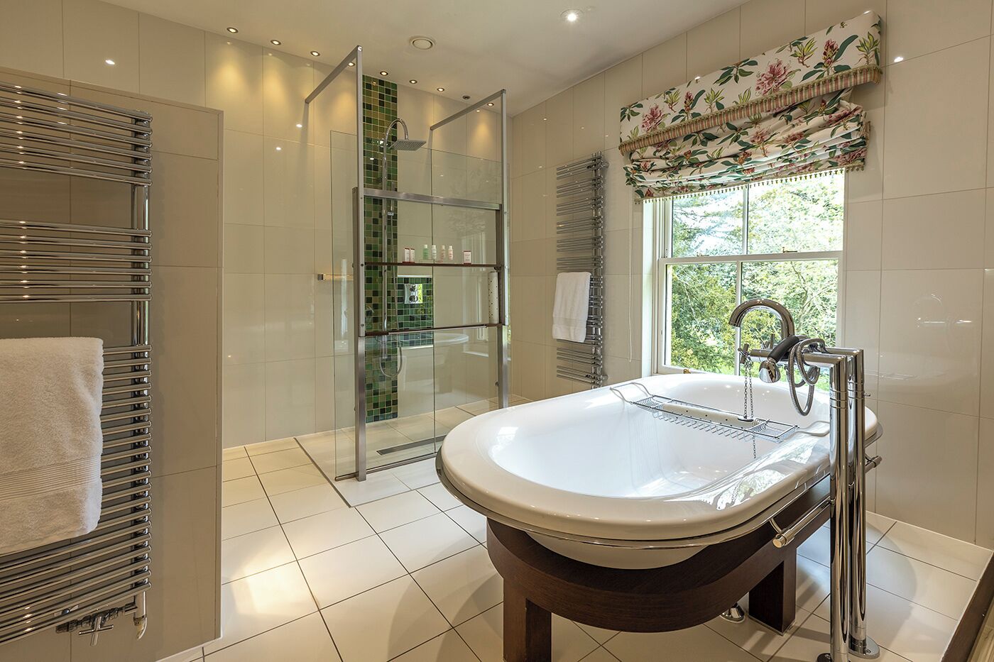 Un baño moderno con ducha de vidrio, una bañera independiente y una ventana con cortina floral.