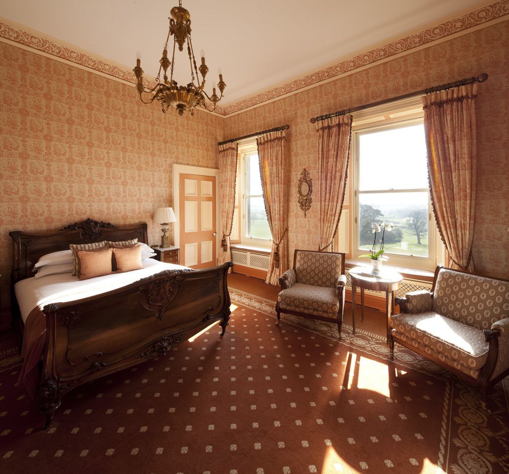 A spacious bedroom with a large bed, a sitting area with a chair and a small table, and a window with curtains.