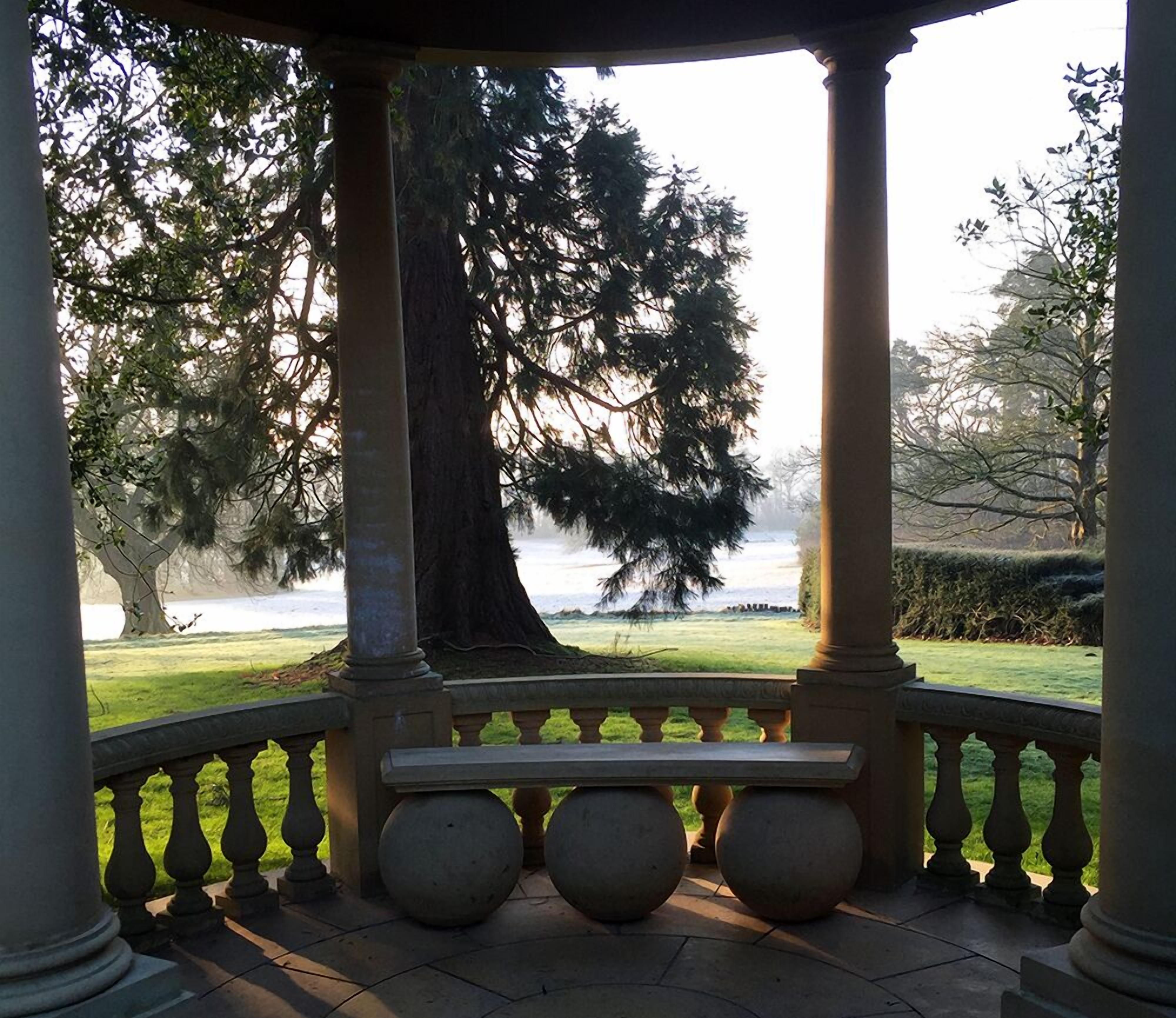Un mirador con banco, columnas y vistas a un lago y árboles.