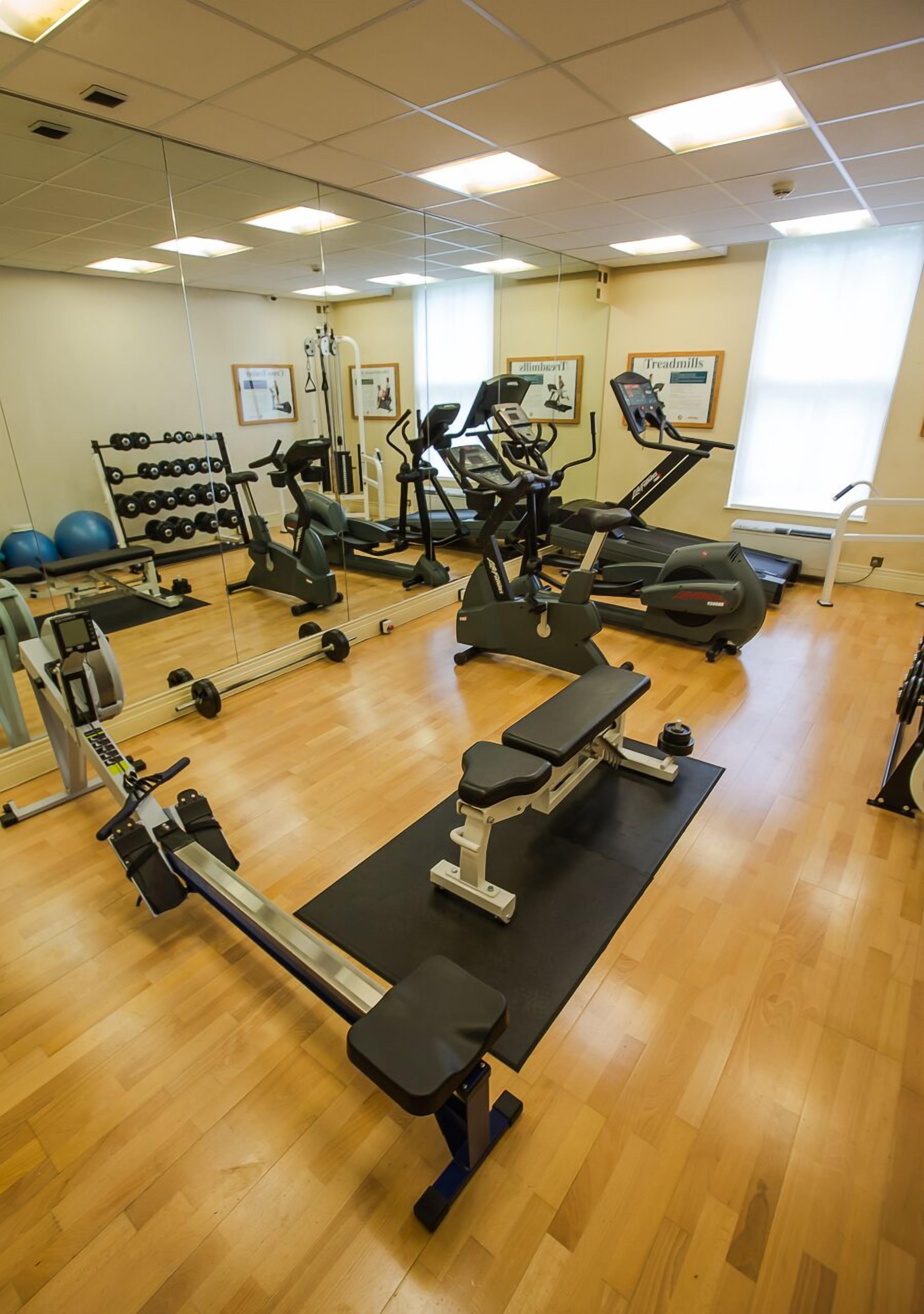 Un gimnasio con diverso equipo de ejercicio, incluyendo cintas de correr y máquinas de pesas, y piso de madera.