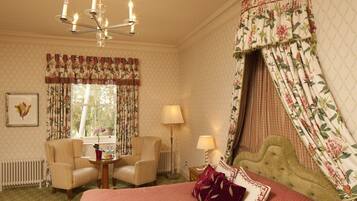 A hotel room with a bed, two armchairs, a small table, a lamp, and a chandelier.