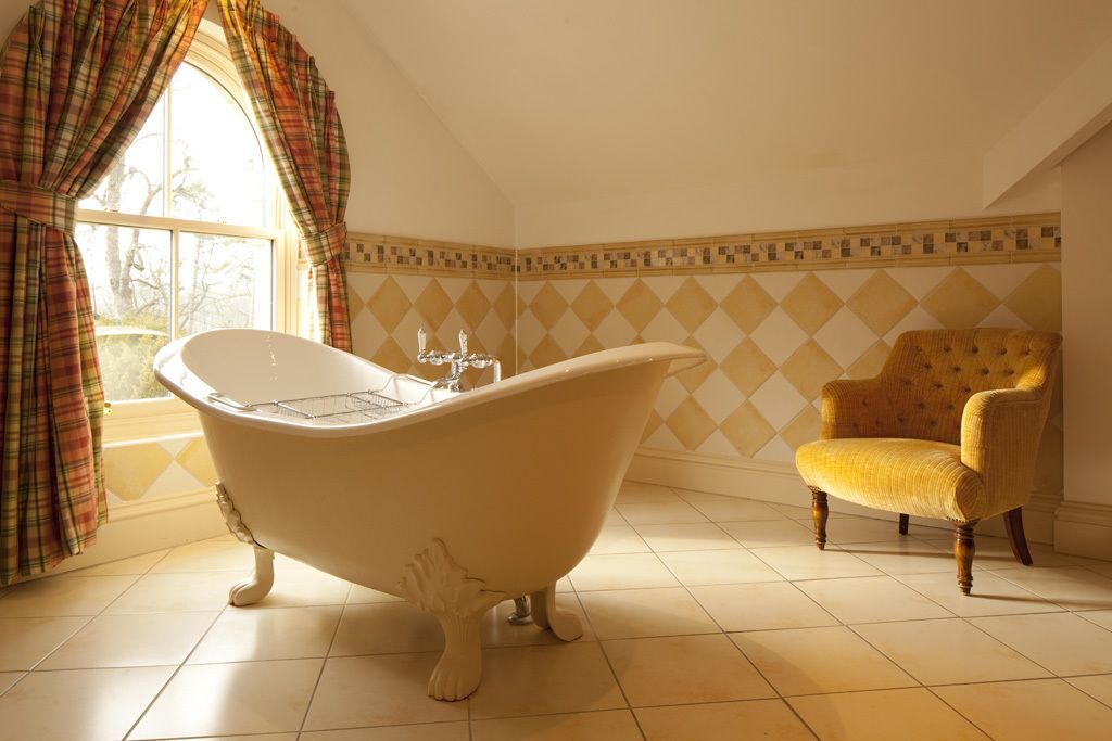 A bathroom with a clawfoot bathtub, a yellow armchair, and a window with plaid curtains.
