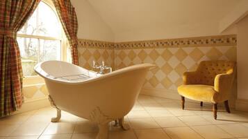 A bathroom with a clawfoot bathtub, a yellow armchair, and a window with plaid curtains.