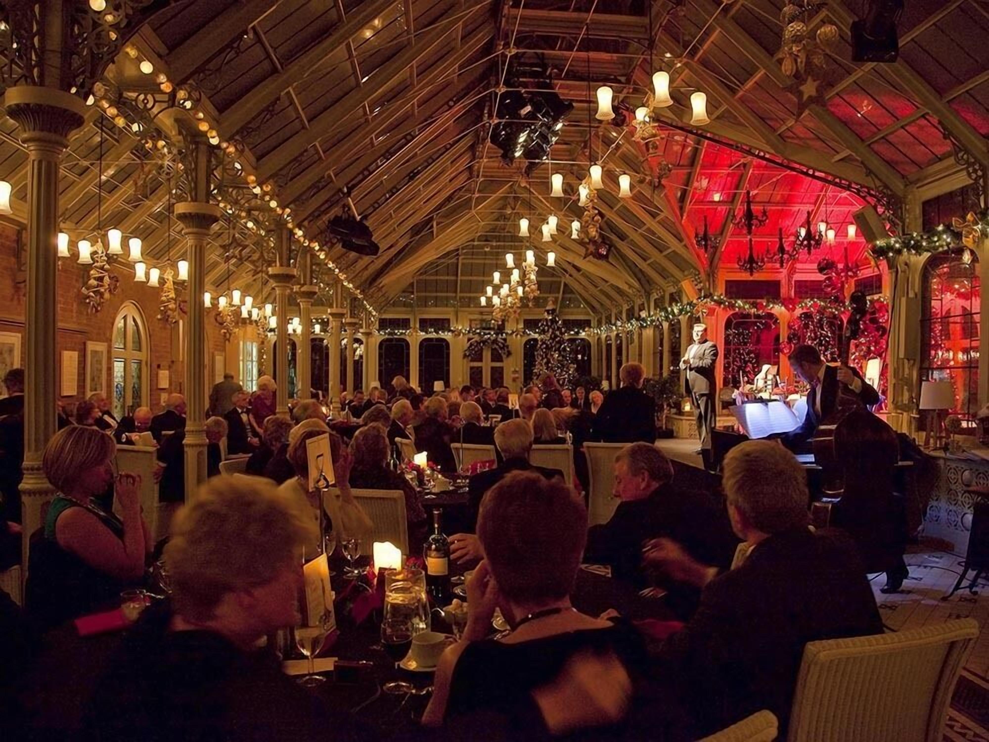 Ein geräumiger, elegant dekorierter Saal mit hohen Decken und aufwendigen Kronleuchtern, der eine Bühne für Aufführungen bietet.