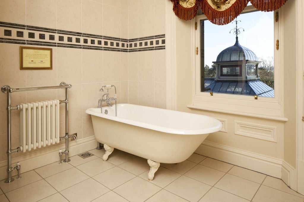 A bathroom with a freestanding bathtub, a radiator, and a window with a view of a dome structure.