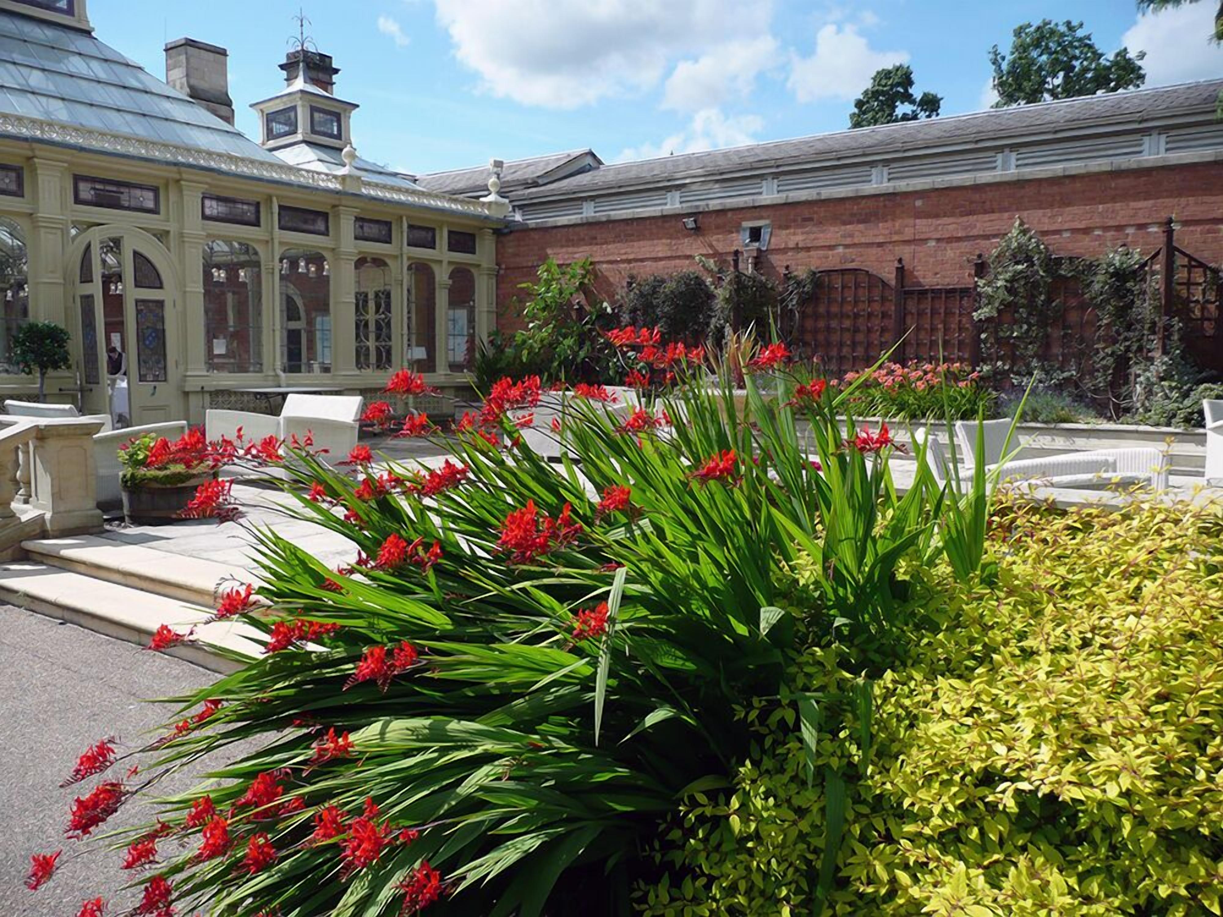Een gebouw met een glazen conservatorium, rode bloemen en een bakstenen muur.